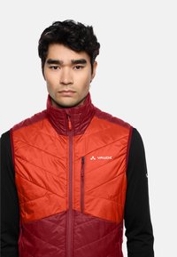 Gilet imbottito arancione e bordeaux, con trapuntatura diagonale, colletto alto e tasca sul petto con zip e logo brandizzato.