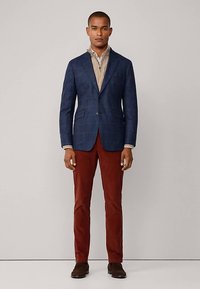 Sako tamnoplavih ćelija, bež košulja, smeđe manšestrene hlače i smeđe cipele. Strukturirani dizajn s reverima i dva prednja džepa.