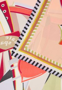 Zblízka barevná látka s geometrickými a květinovými vzory v červené, růžové, zelené a černé barvě se pruhovaným okrajem.