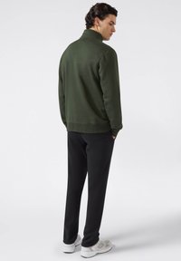 Donkergroen sweatshirt met een kraag, gecombineerd met zwarte broek. Het model draagt witte en grijze sneakers, gezien vanuit de achterkant.