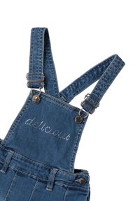 Pantalones de mezclilla con tirantes ajustables y hebillas de metal, presentando el texto "delicioso" en strass en el pecho.