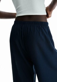 Tamno modre hlače širokega kroja z elastičnim pasom. Gladka tekstura, lahka tkanina. Brez vidnih žepov ali vzorcev.