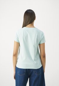 Mint vihreä lyhythihainen t-paita pyöreällä kaula-aukolla, valmistettu pehmeästä kankaasta, yhdistettyinä löysiin tummansinisiin farkkuihin.