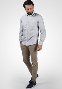 Lyseblå og hvitstripet langermet skjorte med knappestolpe, kombinert med beige slim-fit bukser og marineblå sneakers.
