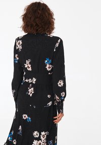 Black floral dress featuring long sleeves, a cinched waist, and various pastel flowers in pink and blue against a textured background.