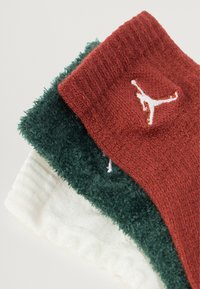 Tres pares de calcetines de toalla: uno rojo con un logo blanco, uno verde oscuro y uno blanco con un puño texturizado.