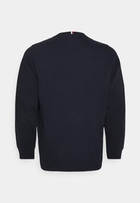 Granatowy sweter z długim rękawem z prążkowanym dekoltem w serek i mankietami, z małym czerwono-białym paskiem na karku.