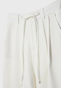 Witte op maat gemaakte broek met een trekkoord in de taille, plooien en zijzakken. Het materiaal lijkt glad met een licht matte afwerking.