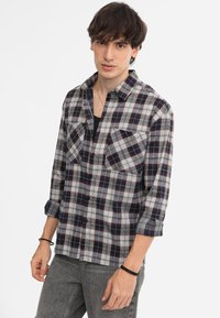 Camicia a scacchi grigia, blu navy e rossa; presenta due tasche sul petto, colletto e maniche arrotolate. Realizzata in tessuto tessuto.