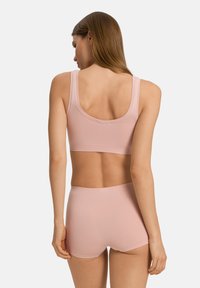 Ljusrosa sömlös bralette med breda axelband och matchande högmidjade shorts, med en slät yta och minimalistisk design.