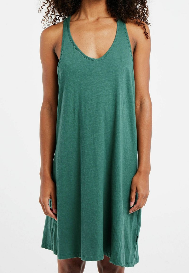 Femme portant une robe verte sans manches longueur genou avec décolleté en V et coupe ample sur fond blanc uni.