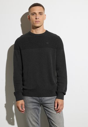 Dunkelgrauer Strickpullover mit strukturiertem Oberteil, Rundhalsausschnitt und Markenlogo auf der Brust. Slim-Fit, kombiniert mit hellgrauen Jeans.