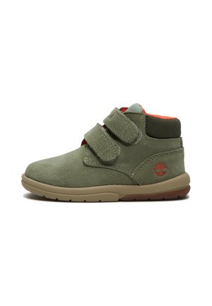 Zapato de niño tipo botín de ante verde con dos correas de velcro, suela beige, cuello acolchado y logotipo rojo en el talón.