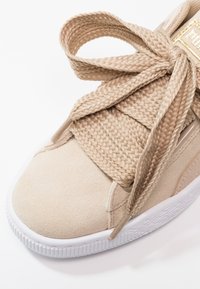 Sneakers en daim beige avec des lacets épais tressés noués en nœud sur une semelle en caoutchouc blanc.