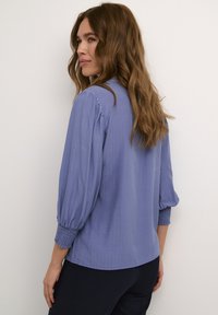 Hellbluse mit Puffärmeln aus strukturiertem Stoff und gerafften Bündchen. Gerader Saum und lockere Passform. Schlichtes Design ohne Muster.