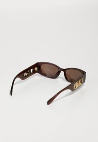 Ochelari de soare din plastic maro, cu lentile întunecate, având accente aurii pe brațe și un design distinct, evidențiind un detaliu cu logo.