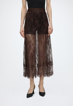 Haut noir sans manches avec une jupe en dentelle marron foncé transparente à taille haute révélant un short intérieur, associé à des chaussures noires à talons.