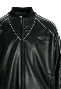 Chaqueta bomber de cuero sintético negro con acentos de ribete blanco, cierre de cremallera en la parte delantera y un bolsillo en el pecho con botones a presión y etiqueta de marca.