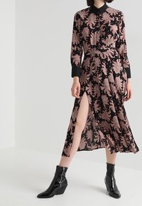 Svart långärmad klänning med rosa blommönster, krage och framsplit. Bärs med blanka svarta ankelstövlar med kilklack.