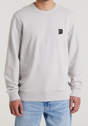 Sweat-shirt gris clair avec un col rond côtelé, des manches longues et un petit logo noir sur la poitrine. Texture douce et coupe régulière.