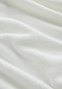 Weißer texturierter Stoff mit einer weichen, luxuriösen Haptik, der ein dezentes Webmuster und sanfte Falten aufweist, die Tiefe und Dimension erzeugen.