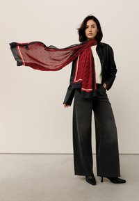 Silk scarf featuring a red geometric pattern with a navy border; worn with a black leather jacket and wide-leg gray jeans.