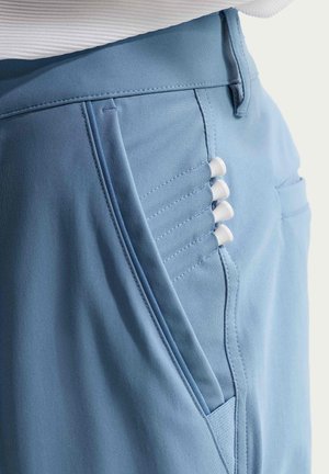 Lähikuva sinisestä housuntaskusta, johon on työnnetty neljä valkoista golf-tikkua saumoihin taskun sivulla.