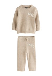 Bežani pleteni komplet džemper i hlače s natpisom "NYC" u bijeloj boji na prsima i gornjem dijelu bedra, s rebrastim manžetama i pojasom na vezanje.