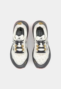 Witte en grijze mesh sportschoenen met een zwarte rubberen zool, gele veters en een contrasterend logo. Voorzien van een versterkte neus en een gestructureerd ontwerp.