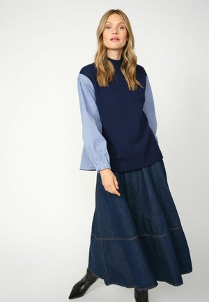 Maglione navy a maglia con maniche lunghe a righe blu e bianche, abbinato a una gonna di jeans scuri e fluidi e stivaletti neri alla caviglia.