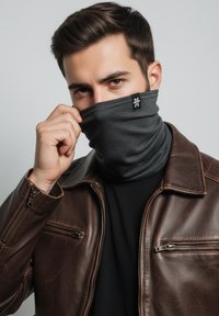 Black neck gaiter made of soft, textured fabric, worn by a model with a brown leather jacket, features a small white logo on the side.