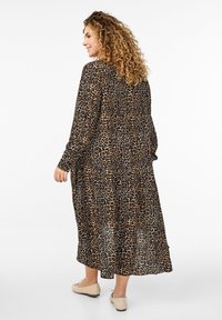 Langes, locker sitzendes Kleid mit Leopardenmuster, das lange Ärmel und einen fließenden Saum hat. Hergestellt aus leichtem Stoff in Beige und Schwarz.