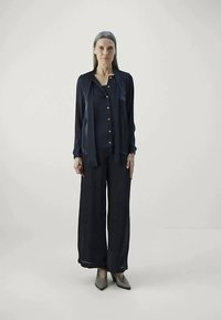 Navy silk blouse with button front, paired with wide-leg trousers. Both feature a smooth texture, complemented by neutral-colored shoes.