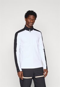 Valge tõmblukuga pikka varrukatopper, millel on mustad aktsendid õlgadel ja varrukatel, valmistatud siledast ja kergest kangast.