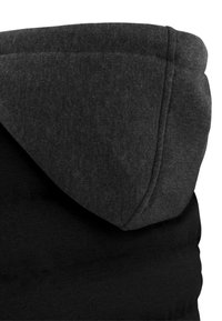 Schwarzer Hoodie mit einer grauen Kapuze. Der Stoff ist glatt und strukturiert, mit einem gestalteten Design und sichtbaren Nähdetails entlang der Kanten.