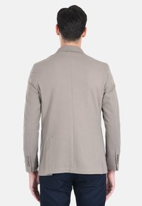 Blazer beige con texture, dal taglio sartoriale, colletto a rever, due tasche laterali e polsini abbottonati, abbinato a pantaloni scuri.