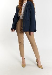 Námořnický voděodolný kabát s kapucí, dvě přední kapsy; v kombinaci s béžovými zúženými kalhotami a tan vysokými podpatky se špičatou špičkou.