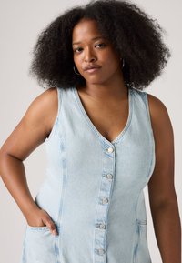 Abito in denim blu chiaro senza maniche con scollatura a V, bottoni frontali e tasche laterali. Tessuto morbido e design aderente.