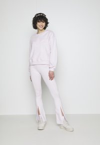 Gaiši rozā džemperis ar izvirzītu logo un atbilstošas formas bikses ar sānu šķēlumiem. Izgatavots no mīkstas kokvilnas maisījuma. Baltas tenisa kedas.