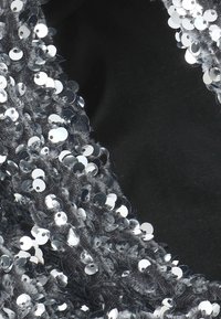 Il tessuto grigio presenta densi paillettes argentate rotonde con una superficie lucida, creando un motivo testurizzato su uno sfondo nero.