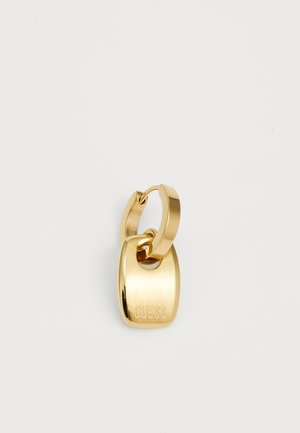 Gullig nøkkelring i gull med en glatt, metallisk overflate og et rektangulært merke gravert med "GUESS." Fester seg med en sirkulær ring.