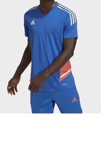 Modré sportovní tričko s výstřihem do V, které má bílé pruhy na ramenou a červený akcent na boku. Vyrobeno z prodyšného materiálu.