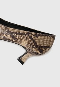 Python-print korkeakorkoinen kenkä, jossa on terävä kärki, musta kantapää, teksturoitu pinta ja yhdistelmä ruskeita ja beigejä sävyjä.