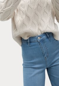Pull en maille crémeuse épaisse avec motif en losanges, associé à un jean taille haute bleu clair avec un bouton argenté et une finition élégante.