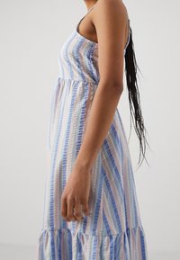 Randig klänning i blå, rosa och vita nyanser. En figurnära överdel övergår till en utsvängd kjol med en volangnedsänkning. Justerbara axelband.