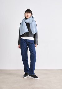 Ljust blått texturerat scarv draperat över en svart läderjacka, bärs med en vit skjorta och blå jeans, som fulländar den avslappnade looken med svarta sneakers.