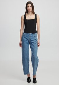 Top senza maniche nero a scollo quadrato abbinato a jeans dritti a vita alta di colore blu chiaro e scarpe slip-on nere. Design semplice, materiale in cotone.
