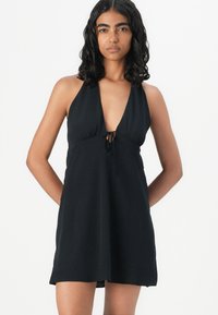 Black halter dress with a plunging neckline, gathered waist, and front drawstring accent. Made of soft, smooth fabric. Knee-length design.
