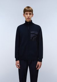 Mörkblå stickad zip-jacka med hög krage, med en framfick i en glänsande tyg, ribbade ärmslut och nederkant. Slät textur.