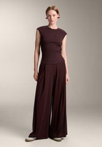 Burgunderfärgad ribbade topp med korta ärmar, kombinerad med vida byxor i samma färg, med en mjuk textur och avslappnad passform.